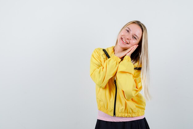 Young lady in t-shirt, jacket leaning cheek on hands and looking positive