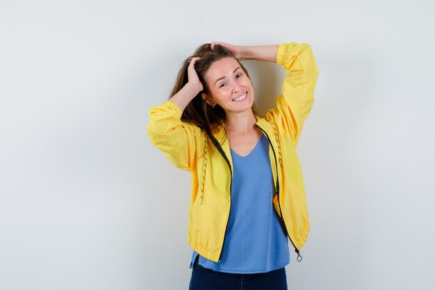 Young lady in t-shirt, jacket posing while holding hands on head and looking dizzy, front view.