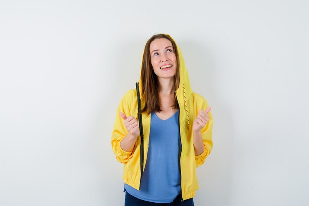 Young lady in t-shirt, jacket showing double thumbs up and looking confident , front view.