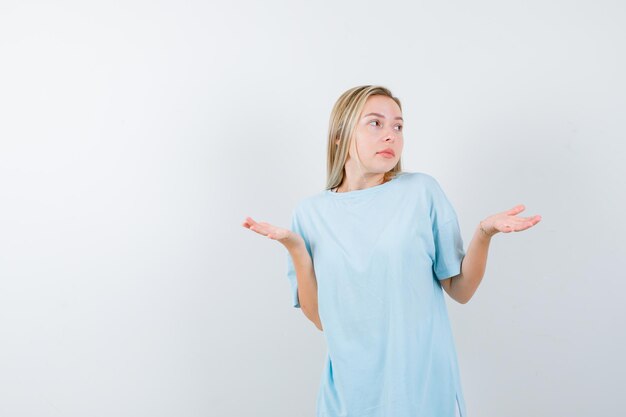 Young lady in t-shirt making scales gesture and looking hesitant isolated