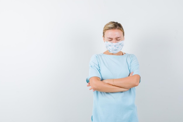 Young lady in t-shirt, mask standing with crossed arms and looking sorrowful