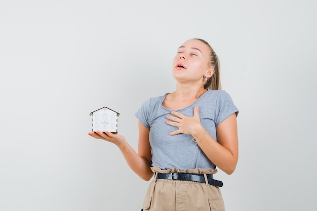 Free Photo young lady in t-shirt and pants holding house model and looking grateful