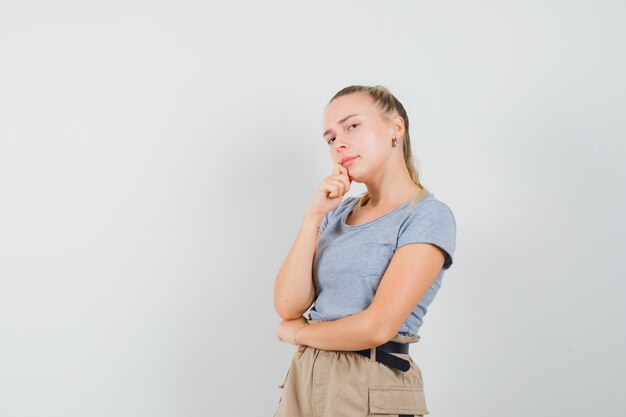 Young lady in t-shirt and pants standing in thinking pose and looking sensible