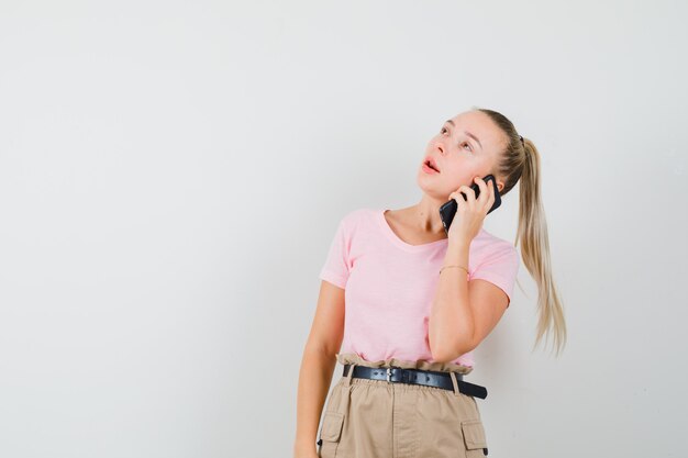 Young lady in t-shirt and pants talking on mobile phone and looking indecisive