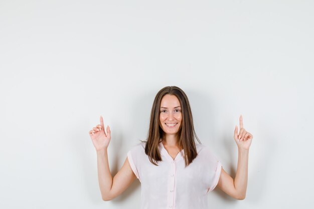 Young lady in t-shirt pointing up and looking merry , front view.