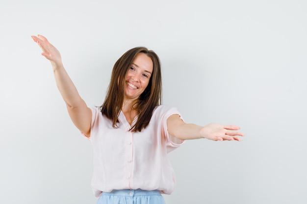 Young lady in t-shirt, skirt opening arms for hug and looking friendly , front view.