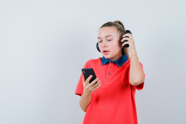 Young lady taking off headphones, using mobile phone in t-shirt