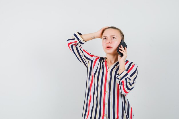 Free Photo young lady talking on mobile phone in striped shirt and looking pensive