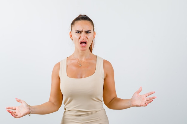 Young lady in tank top showing helpless gesture and looking puzzled , front view.