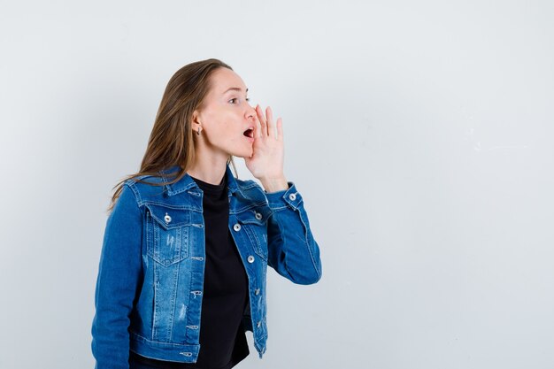 Young lady telling secret with hand near mouth in blouse , front view.