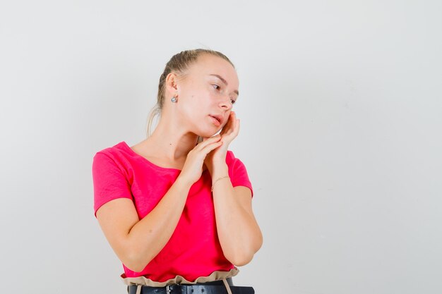 Young lady touching her face skin on cheek in pink t-shirt and looking cute