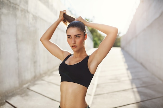 Free Photo young lady tying her hair just before her everyday everning workout on a sunny summer day in concrete jungle. urban sport concept.