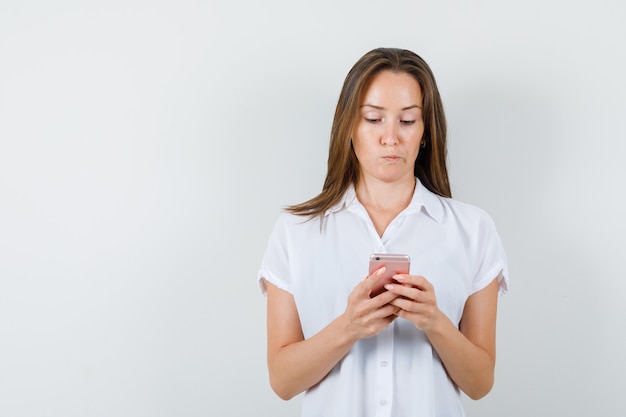 Young lady typing something on phone in white blouse and looking puzzled