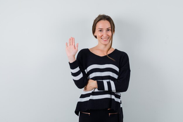 Young lady waving hand to say hello in shirt and looking jovial