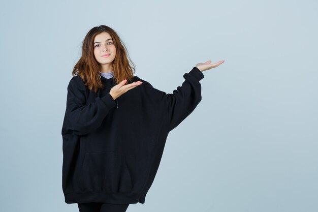 Young lady welcoming in oversized hoodie, pants and looking confident , front view.