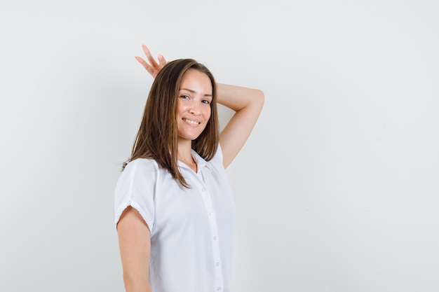 Young lady in white blouse making bunny gesture on her head and looking pleased