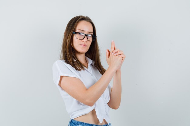 Young lady in white blouse showing pistol gesture and looking focused , front view.