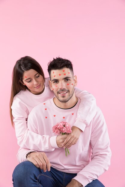 Young lady with flowers hugging guy with paper hearts on face 