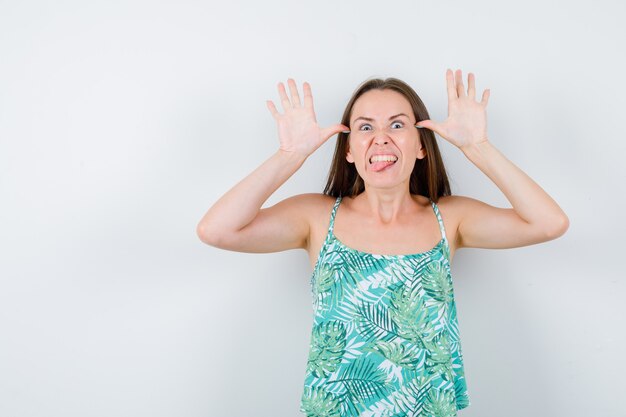 Young lady with hands near head as ears, sticking tongue out and looking crazy , front view.