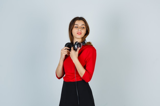 Free photo young lady with headphones posing while looking away in red blouse