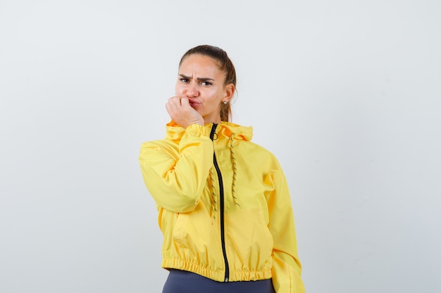 Young lady in yellow jacket keeping hand on chin and looking dissatisfied , front view.