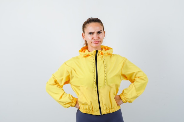 Free photo young lady in yellow jacket with hands on waist and looking displeased , front view.