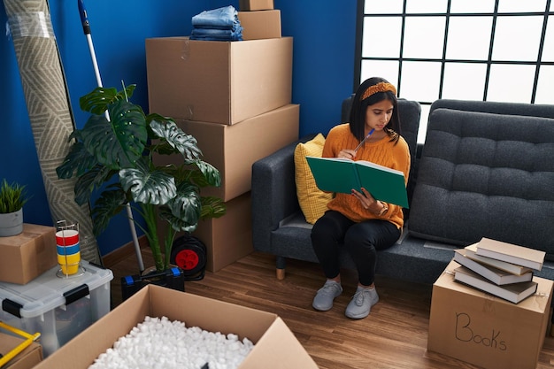 Free photo young latin woman reading book sitting on sofa at new home