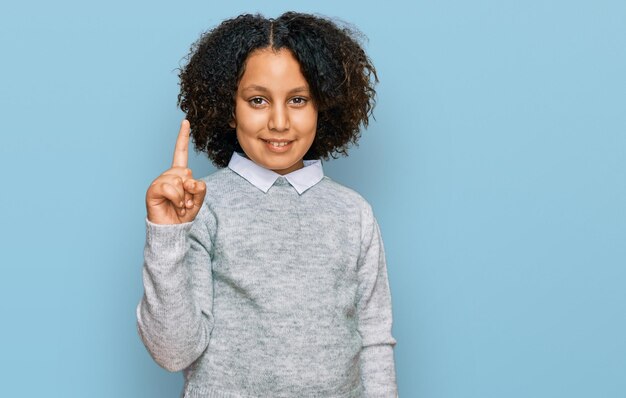 Young little girl with afro hair wearing casual clothes showing and pointing up with finger number one while smiling confident and happy