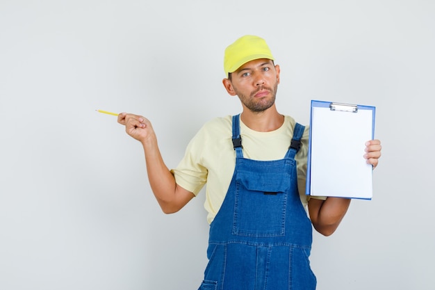 Free photo young loader holding clipboard and pointing to side in uniform , front view.