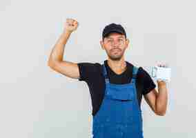 Free photo young loader holding mini clipboard with winner gesture in uniform front view.