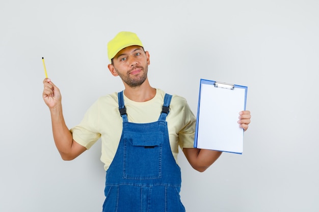 Free photo young loader in uniform holding clipboard and pencil and looking cheery , front view.