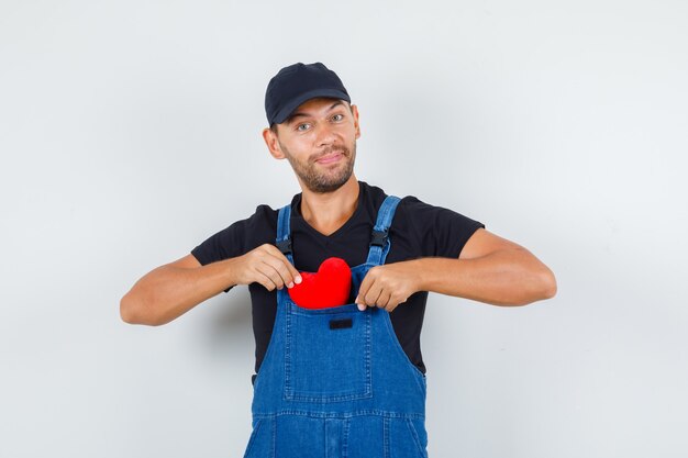 Young loader in uniform putting red heart in his pocket and looking cheerful , front view.