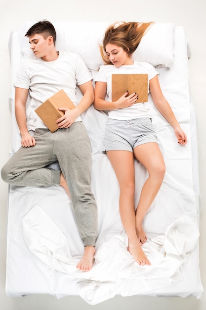 The young lovely couple lying in a bed with books