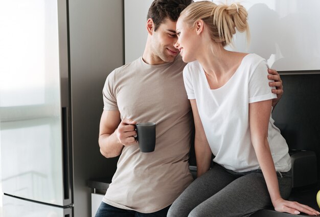 Young lovers enjoying hugging while standing in kitchen