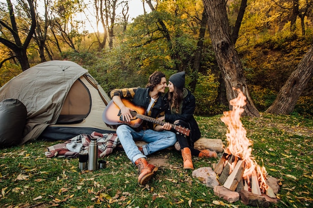 Young loving couple of tourists relaxing near the fire in the nature