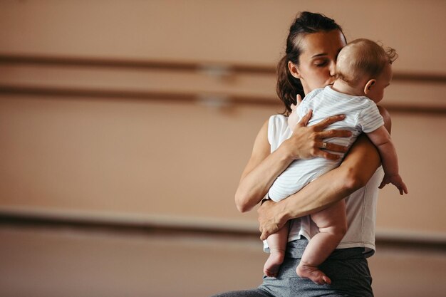 Free Photo young loving mother kissing her baby while holding him during exercise class in health club copy space