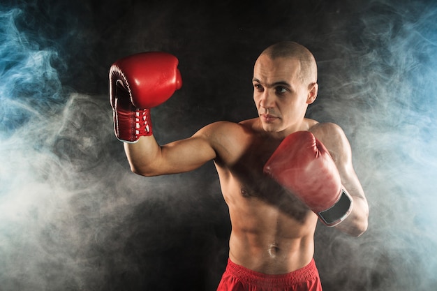 The young male athlete kickboxing on a background of blue smoke