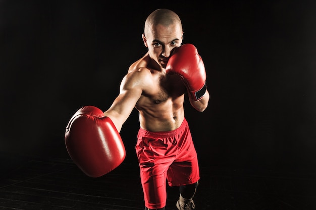 The young male athlete kickboxing on a black background