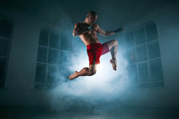 The young male athlete kickboxing on a of blue smoke