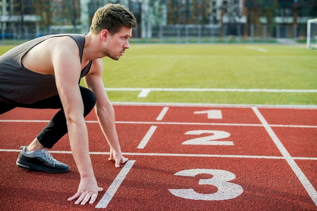 Young male athlete ready to run taking position at the start line