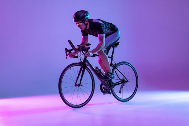 Young male bike rider on bicycle isolated on gradient wall in neon man training and practicing