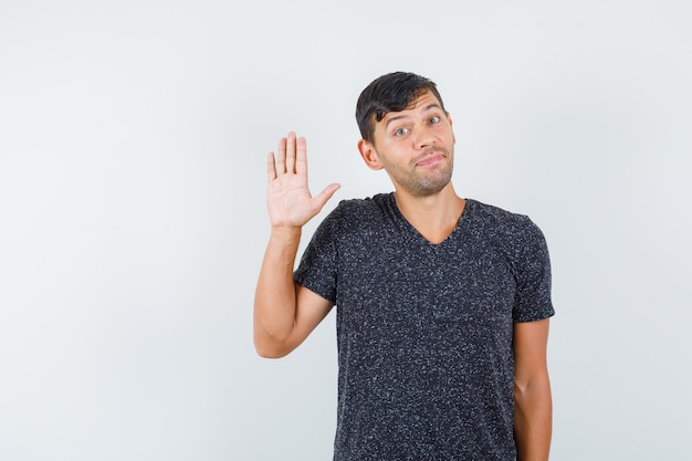 Young male in black t-shirt waving hand for greeting , front view.