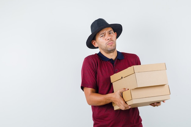 Free Photo young male carrying boxes in red shirt,black hat and looking troubled. front view.