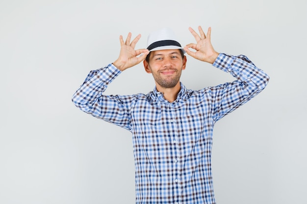 Young male in checked shirt holding his hat and looking merry