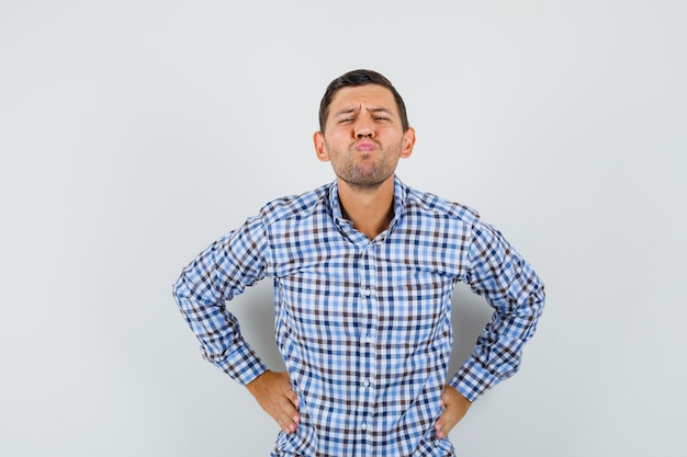 Young male in checked shirt scowling while holding hands on waist