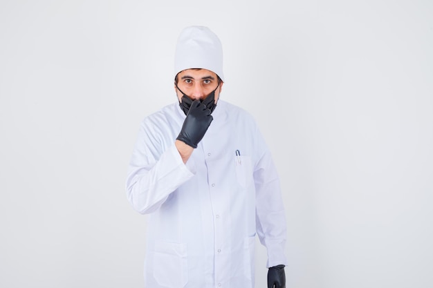 Young male doctor in white uniform opening mask and looking serious , front view.