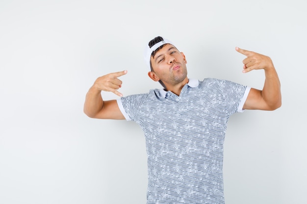 Free photo young male doing rock symbol in t-shirt and cap and looking cool