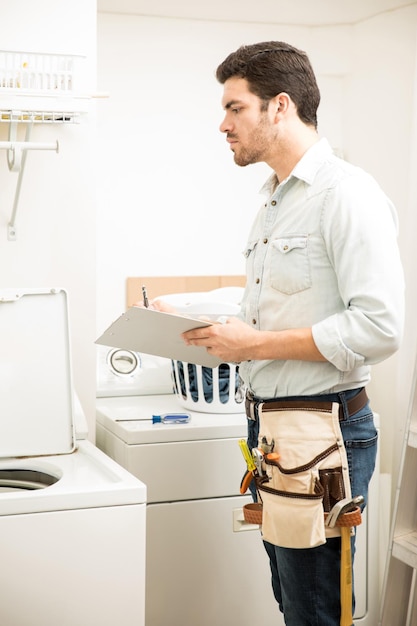 Young male electrician doing some repairs in a laundry room and looking at a washing machine