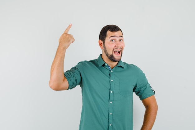 Young male in green shirt pointing up and looking happy , front view.