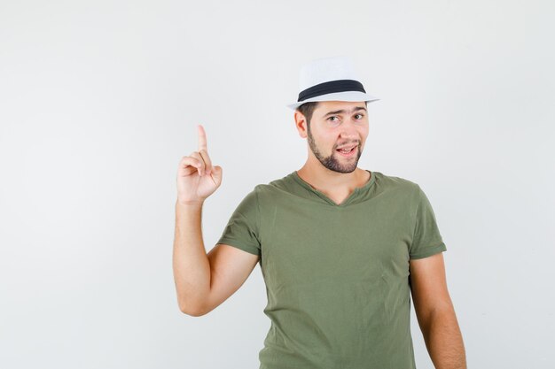 Young male in green t-shirt and hat pointing up and looking confident